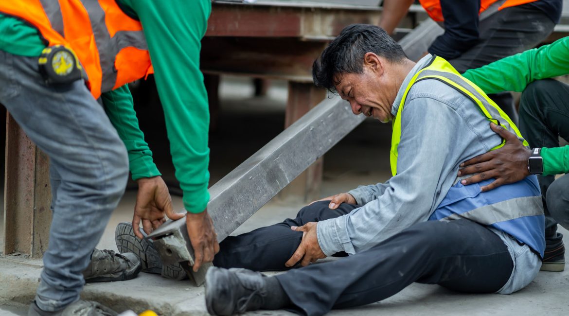 Co-workers assisting an injured worker on the job by lifting a heavy beam off their leg following a workplace accident.
