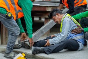 Co-workers assisting an injured worker on the job by lifting a heavy beam off their leg following a workplace accident.